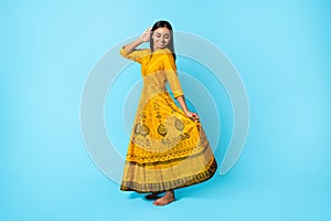 Young Indian Lady Wearing Yellow Traditional Dress Dancing, Blue Background