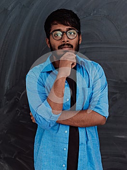 A young Indian man in a blue shirt and glasses poses thoughtfully in front of school board