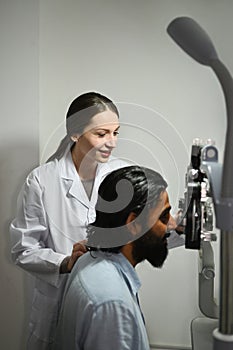 Young Indian man checking eyesight on auto refractor in ophthalmologist clinic. Eye health check and ophthalmology