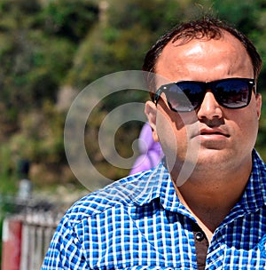 Young Indian man close up, fair skin and dark sun glasses to beat bright summer sun