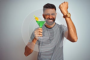 Young indian man drinking cocktail with alcohol standing over isolated white background annoyed and frustrated shouting with