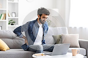 Young indian man experiencing back pain while working on laptop at home