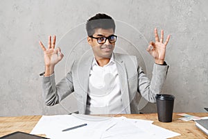 Young indian man gesturing okay sign while working with documents