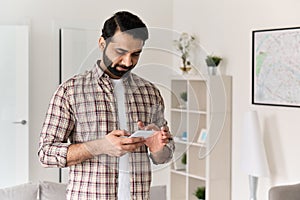 Young indian man holding smartphone using cell phone at home.