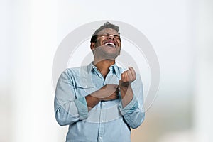 Young indian man is laughing out loud standing on blurred background.