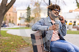 Young indian man sitting in the bench with coffee using mobile phone