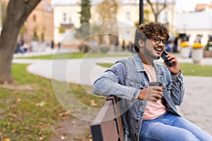 Young indian man sitting in the bench with coffee using mobile phone