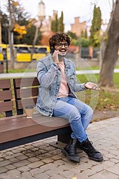 Young indian man sitting in the bench with coffee using mobile phone