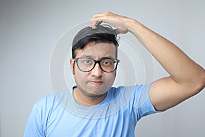 A young indian man in spectacles scratching his head and looking confused and thoughtful