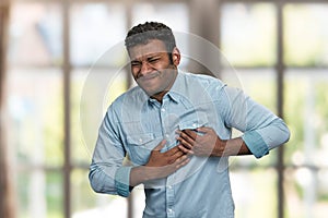 Young indian man suffering from heart ache. Blur interior background.