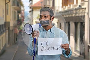 Young indian man with taped mouth unable to speak into megaphone.