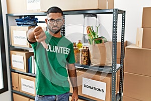 Young indian man volunteer holding donations box looking unhappy and angry showing rejection and negative with thumbs down gesture