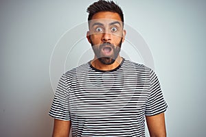 Young indian man wearing black striped t-shirt standing over isolated white background afraid and shocked with surprise