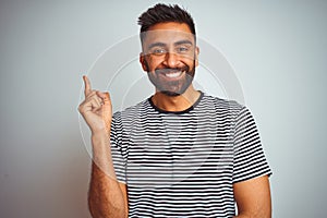 Young indian man wearing black striped t-shirt standing over isolated white background with a big smile on face, pointing with