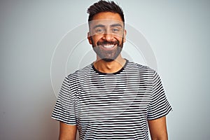 Young indian man wearing black striped t-shirt standing over isolated white background with a happy and cool smile on face