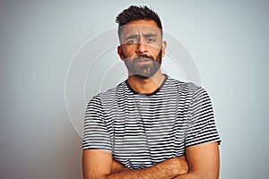 Young indian man wearing black striped t-shirt standing over isolated white background skeptic and nervous, disapproving