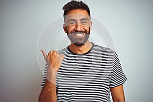 Young indian man wearing black striped t-shirt standing over isolated white background smiling with happy face looking and