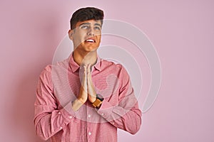 Young indian man wearing elegant shirt standing over isolated pink background begging and praying with hands together with hope