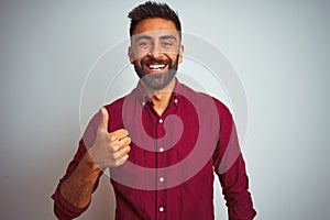 Young indian man wearing red elegant shirt standing over isolated grey background doing happy thumbs up gesture with hand