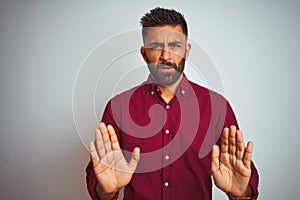 Young indian man wearing red elegant shirt standing over isolated grey background Moving away hands palms showing refusal and