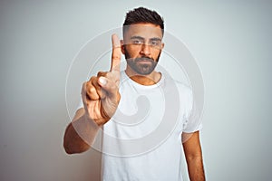 Young indian man wearing t-shirt standing over isolated white background Pointing with finger up and angry expression, showing no