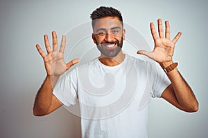 Young indian man wearing t-shirt standing over isolated white background showing and pointing up with fingers number ten while