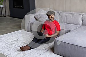 Young indian man working on laptop sittin on floor in living room