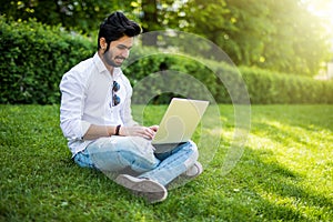 Young indian Student man with a laptop sitting on the grass. Urban style.