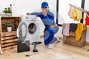 Young indian technician working on washing machine smelling something stinky and disgusting, intolerable smell, holding breath