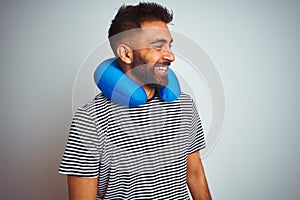Young indian tourist man on travel wearing neckpillow over isolated white background looking away to side with smile on face,