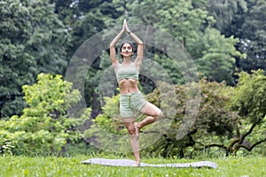 Young Indian woman doing yoga in nature. Standing in a pose with closed eyes, meditating