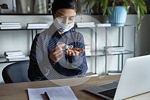 Young Indian woman in face mask cleanse hands with sanitizer