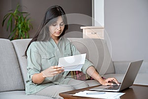 Young indian woman holding letter using laptop paying bill online at home.