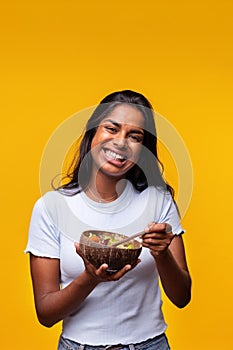 Young Indian woman isolated on yellow background eating healthy salad. Vertical image. Healthy lifestyle