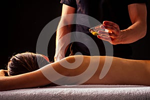 Young indian woman lying on the table and getting ayurvedic massage with organic oil or honeyed in dark room.massagist