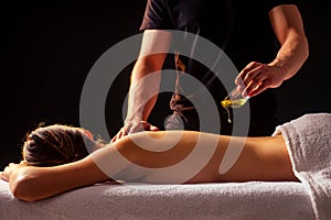 Young indian woman lying on the table and getting ayurvedic massage with organic oil or honeyed in dark room.massagist