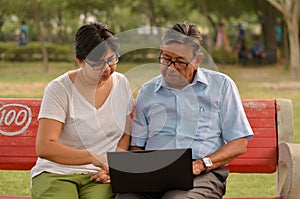 Young Indian woman manager in western formals / shirt helping old Indian man on a laptop promoting digital literacy for elderly in