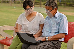 Young Indian woman manager in western formals / shirt helping old Indian man on a laptop promoting digital literacy for elderly in