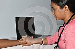 Young Indian woman nurse taking pulse of senior man by fingers isolated on white background. Medical checking on table, selective