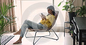 Young Indian woman sit in armchair with modern smart phone