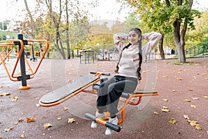 Young Indian woman in sportswear doing sit-ups on an outdoor exercise machine
