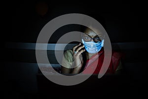 Young indian Woman wearing mask working on her laptop and talking on phone, late night working, freelancer working from home.