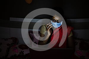 Young indian Woman wearing mask working on her laptop and talking on phone, late night working, freelancer working from home.