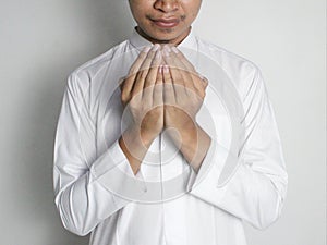 Young Indonesian Muslim man wearing a white robe is raising his hands to pray isolated on white background front view