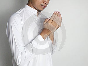 Young Indonesian Muslim man wearing a white robe is raising his hands to pray isolated on white background side view