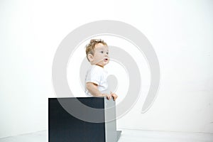 A young infant boy peeking out of a box on a white background