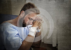Young injured man in hospital room sitting alone in pain worried for his health condition photo