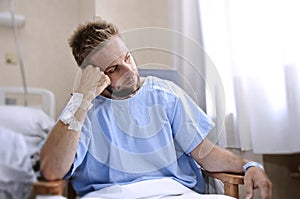 Young injured man in hospital room sitting alone in pain worried for his health condition photo