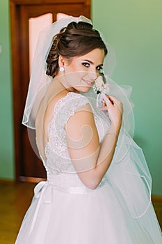 Young innocent bride in white dress posing, holding cute little boutenniere and looking over her shoulder
