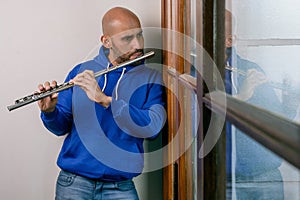 young inspired latin young man playing the flute at home and looking out the window